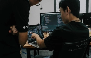 Programista siedzący przed laptopem tłumaczy drugiej osobie kod strony.